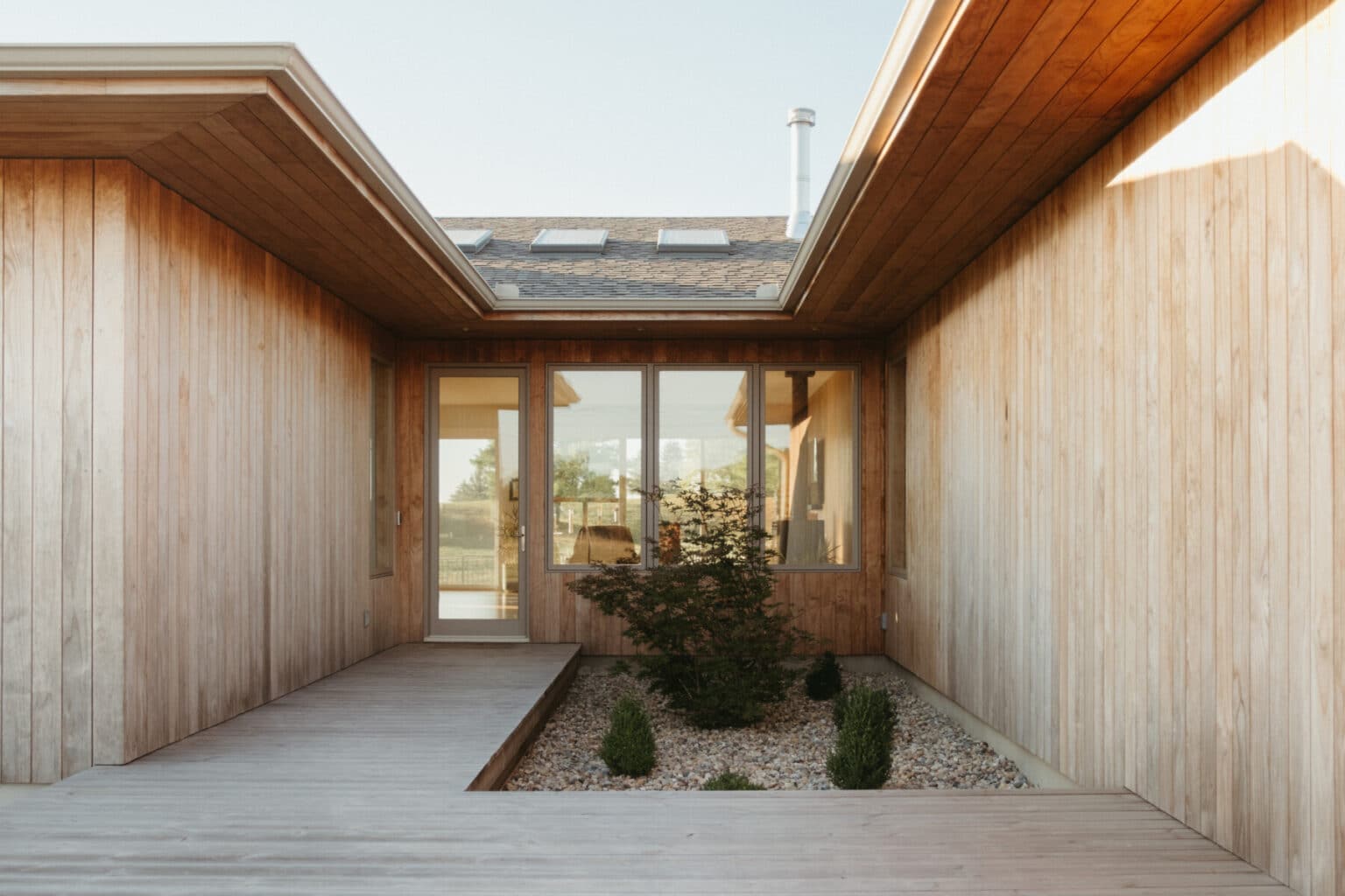 A modern house design Urbana IL, this wooden exterior features a boardwalk entry, large windows, and a small landscaped garden with rocks and shrubs.