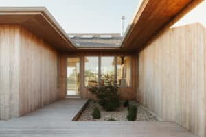 A modern house design Urbana IL, this wooden exterior features a boardwalk entry, large windows, and a small landscaped garden with rocks and shrubs.