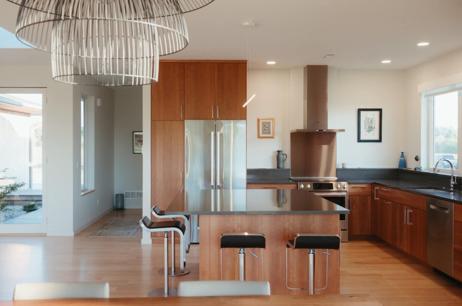 Modern kitchen with wooden cabinets, stainless steel appliances, a large island with two stools, pendant lights, and minimal decor—reflecting modern house design Urbana IL style.