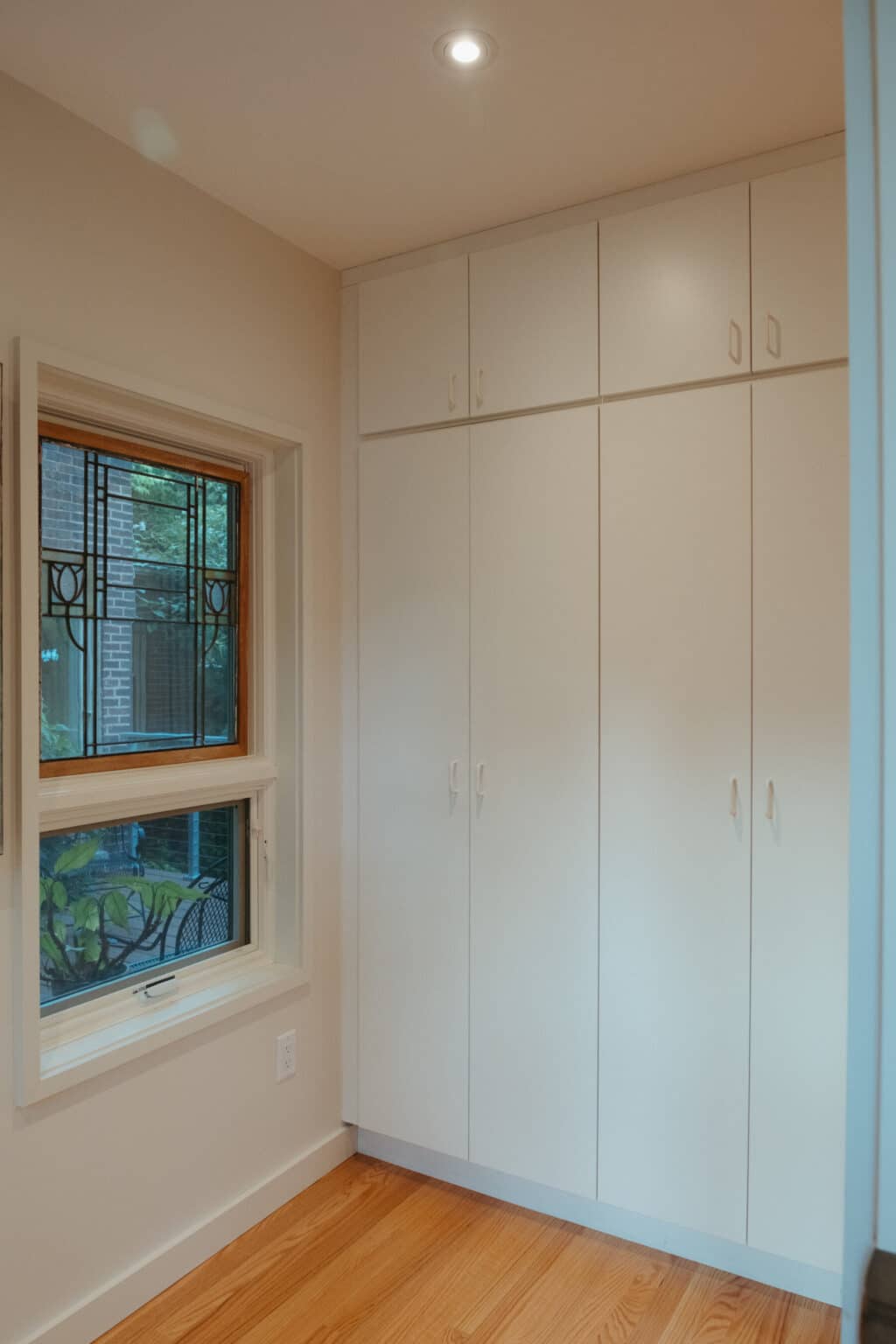 A white built-in closet with multiple cabinets is next to a window with decorative metal bars, set in a room with light-colored walls and wood flooring—an example of Urbana IL home addition design.