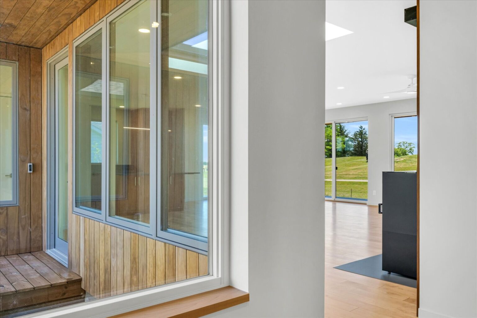 View from inside a modern house design Urbana IL, featuring large windows, wood paneling, and an open living area filled with natural light and scenic outdoor views.