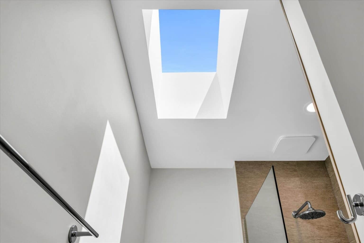View of a bathroom ceiling in a modern house design Urbana IL, featuring a rectangular skylight that lets in daylight, with glimpses of a towel bar, showerhead, and part of the shower enclosure.