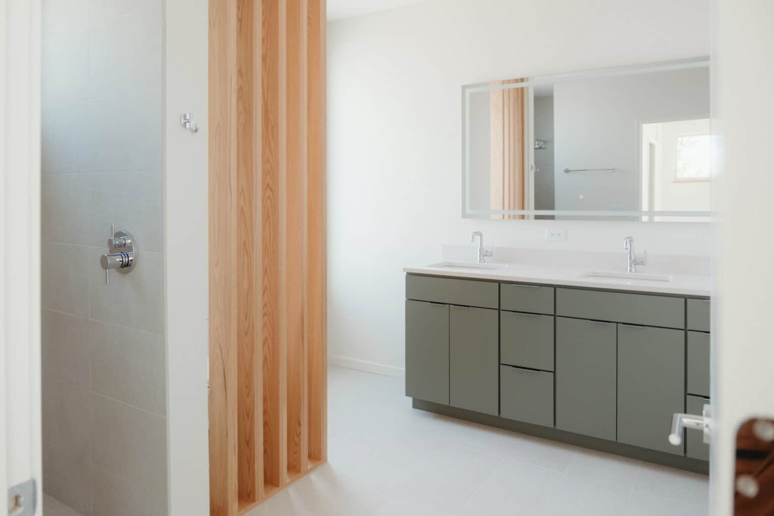 Modern bathroom with a double sink vanity, large mirror, and walk-in shower separated by vertical wooden slats—an elegant touch in custom home design Urbana IL.
