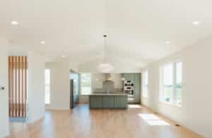 A modern, open-concept kitchen with light wood floors, sage green cabinets, stainless steel appliances, and large windows letting in natural light—perfect for a custom home design in Urbana IL.