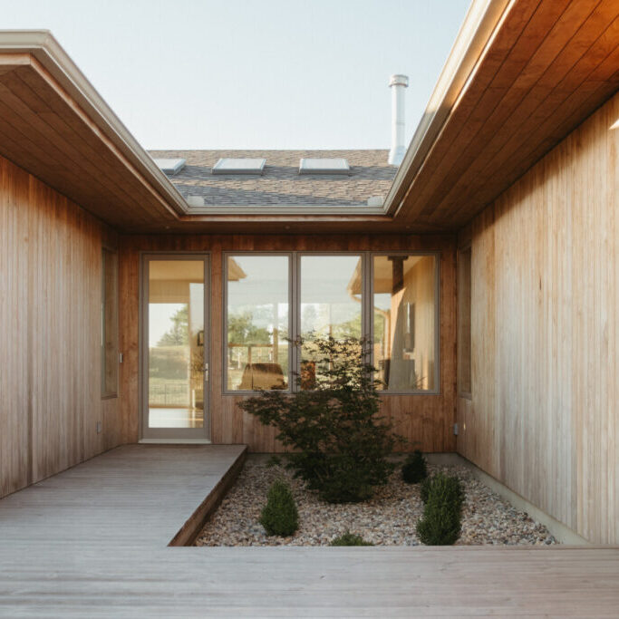 A modern house design Urbana IL, this wooden exterior features a boardwalk entry, large windows, and a small landscaped garden with rocks and shrubs.
